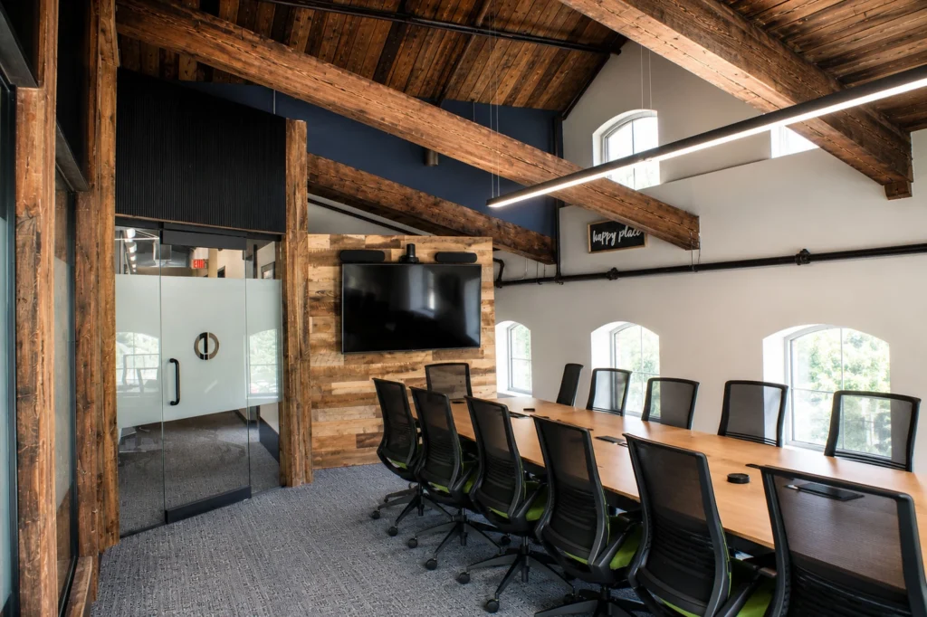 Capital Data meeting space featuring a modern conference table, glass-walled office entrance, exposed timber framing, reclaimed wood accents, and integrated audiovisual technology.