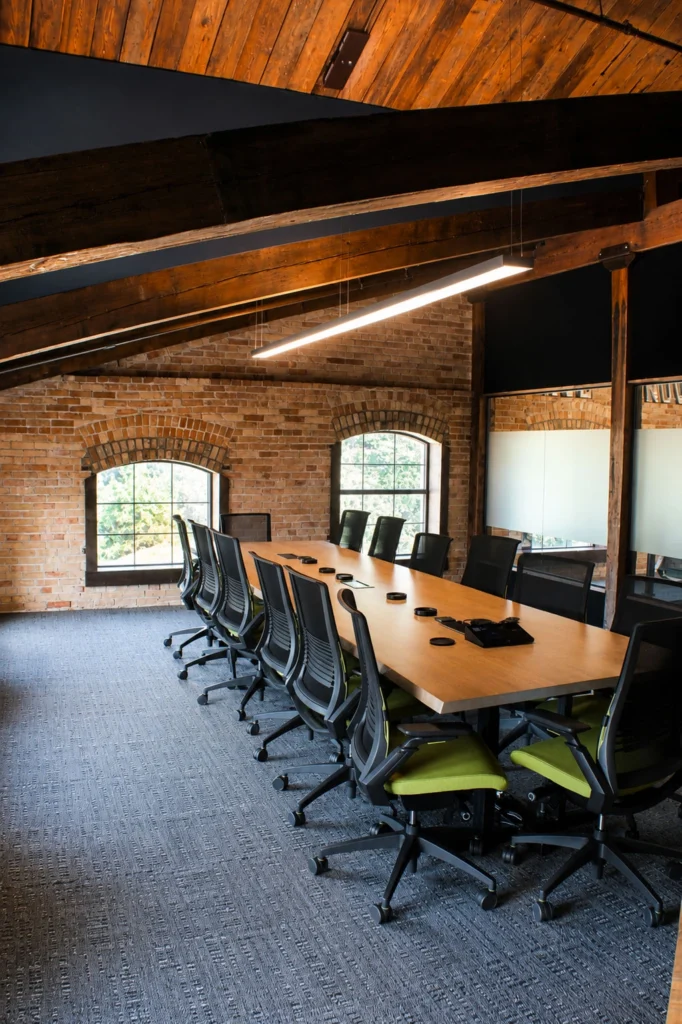 Capital Data conference room with a large collaborative meeting table, ergonomic seating, exposed wood beams, brick walls, and abundant natural light.