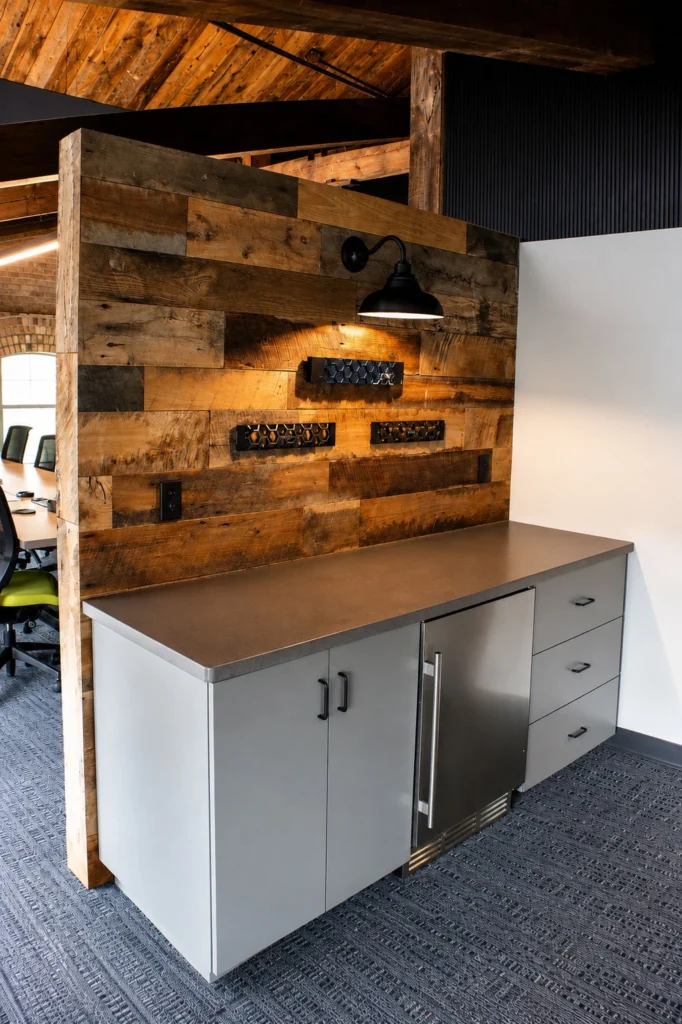 Custom office coffee bar and storage area at Capital Data featuring gray cabinetry, undercounter refrigeration, rustic wood accent walls, and exposed timber beams.