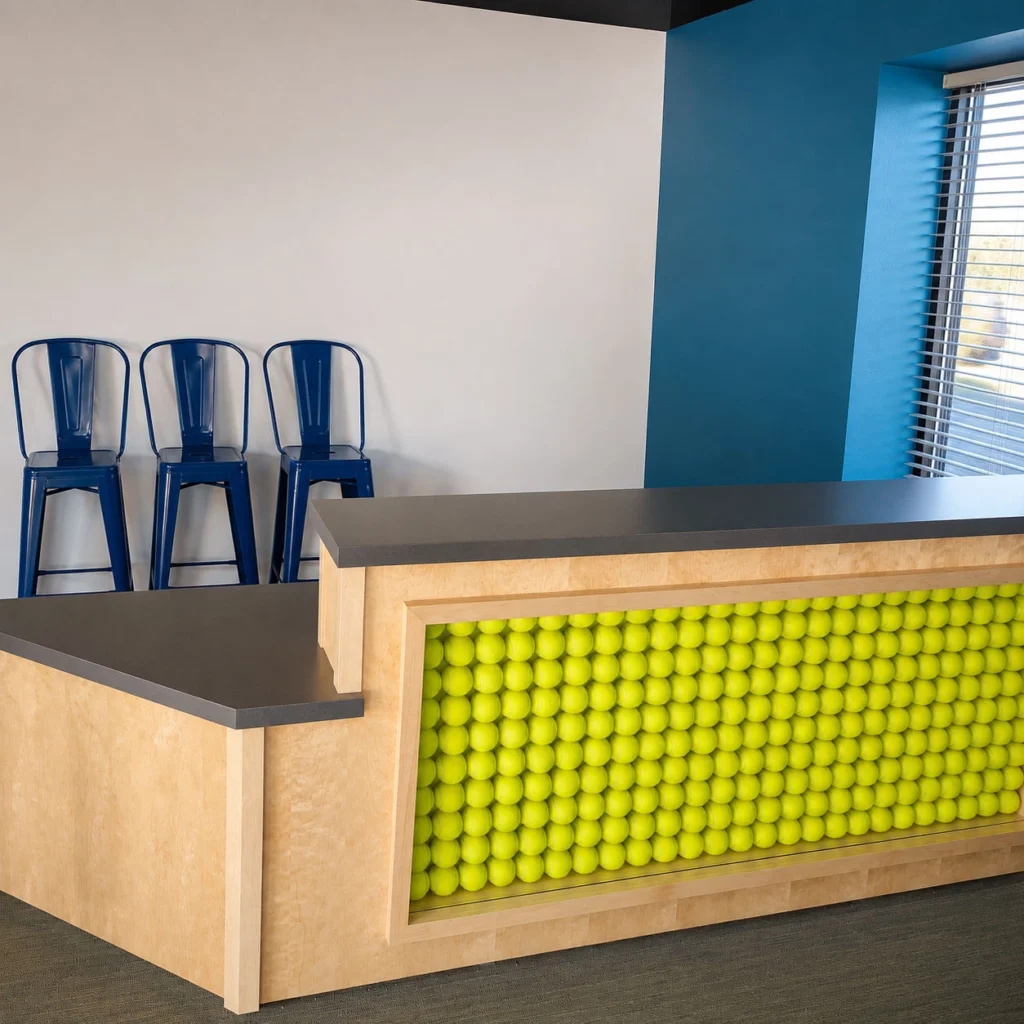 Reception counter at Fetch, Play + Sip showcasing a custom front panel made of bright tennis balls, modern finishes, and vibrant blue accents.