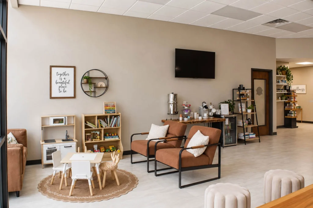 Reception area at Flow Family Chiropractic featuring a custom wood and stone-look check-in desk, illuminated logo, pendant lighting, and warm modern finishes.