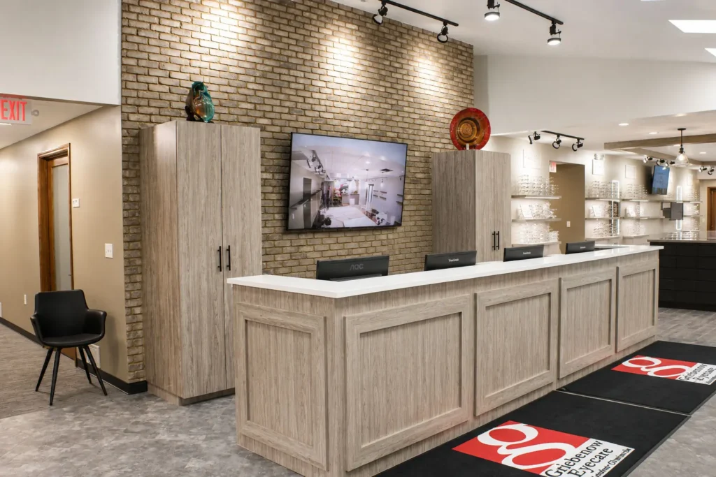Reception area at Griebenow Eye Care in New London showcasing a custom check-in desk, brick accent wall, contemporary finishes, and integrated patient service workspace.