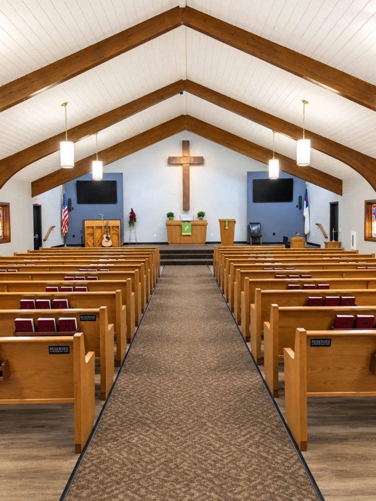 Expanded worship space at St. Paul’s Lutheran Church in Clintonville featuring wooden pews, exposed wood beams, stained-glass windows, pendant lighting, and a vaulted ceiling.