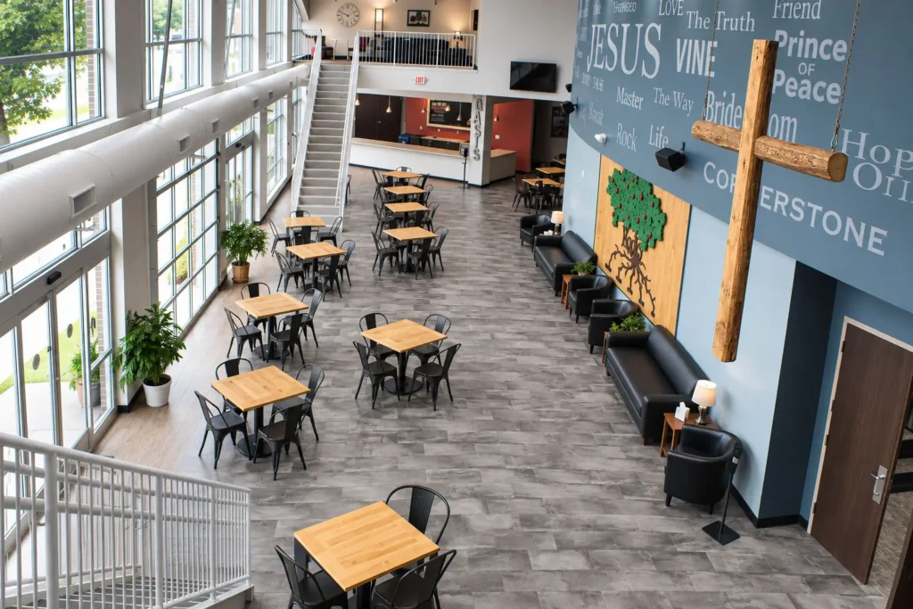Open gathering space at 922 Ministries The Core featuring floor-to-ceiling windows, community seating areas, a large wooden cross, and welcoming spaces designed for fellowship and connection.