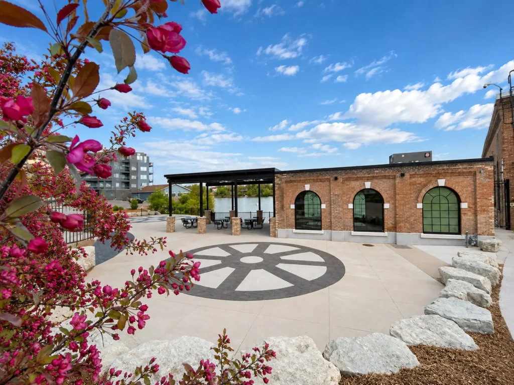 Cedar Overlook in the Village of Kimberly featuring a riverside gathering plaza, decorative paving, landscaped planting beds, restored brick architecture, and a covered pavilion overlooking the Fox River.
